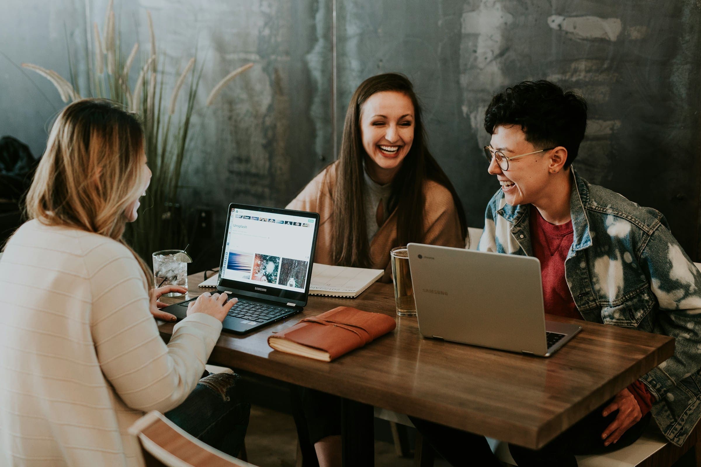 Three people laughing together around a table with laptops