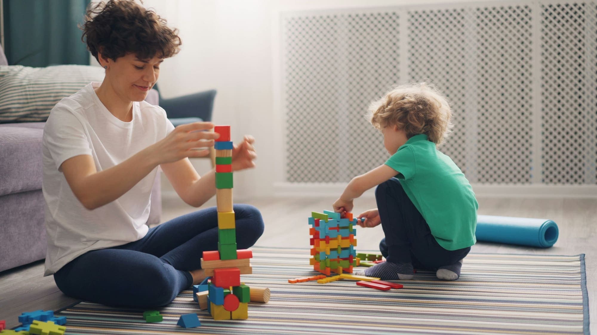 A therapist and a young child building with wooden blocks on the floor