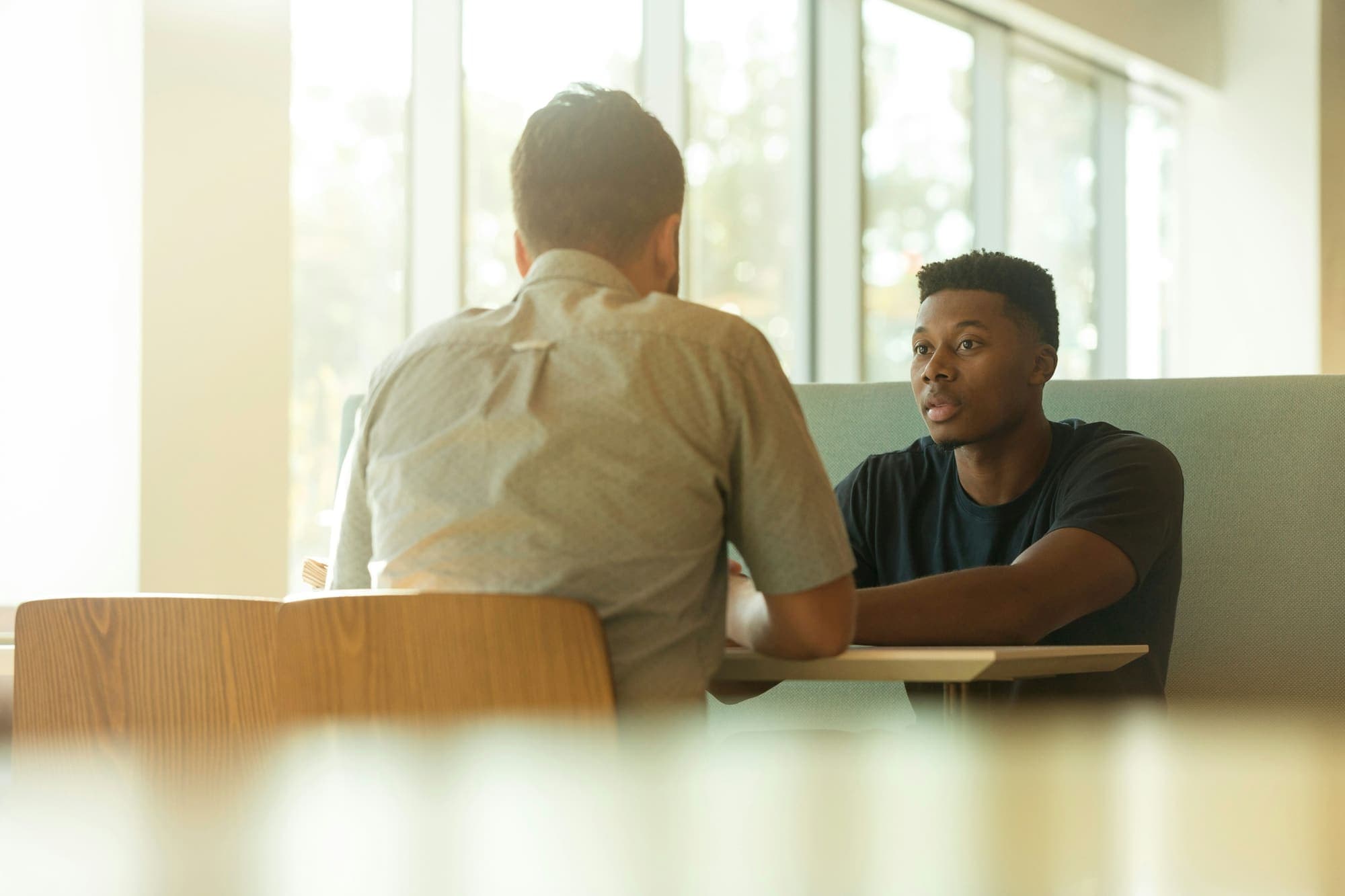 Two people talking across a table in a sunlit room